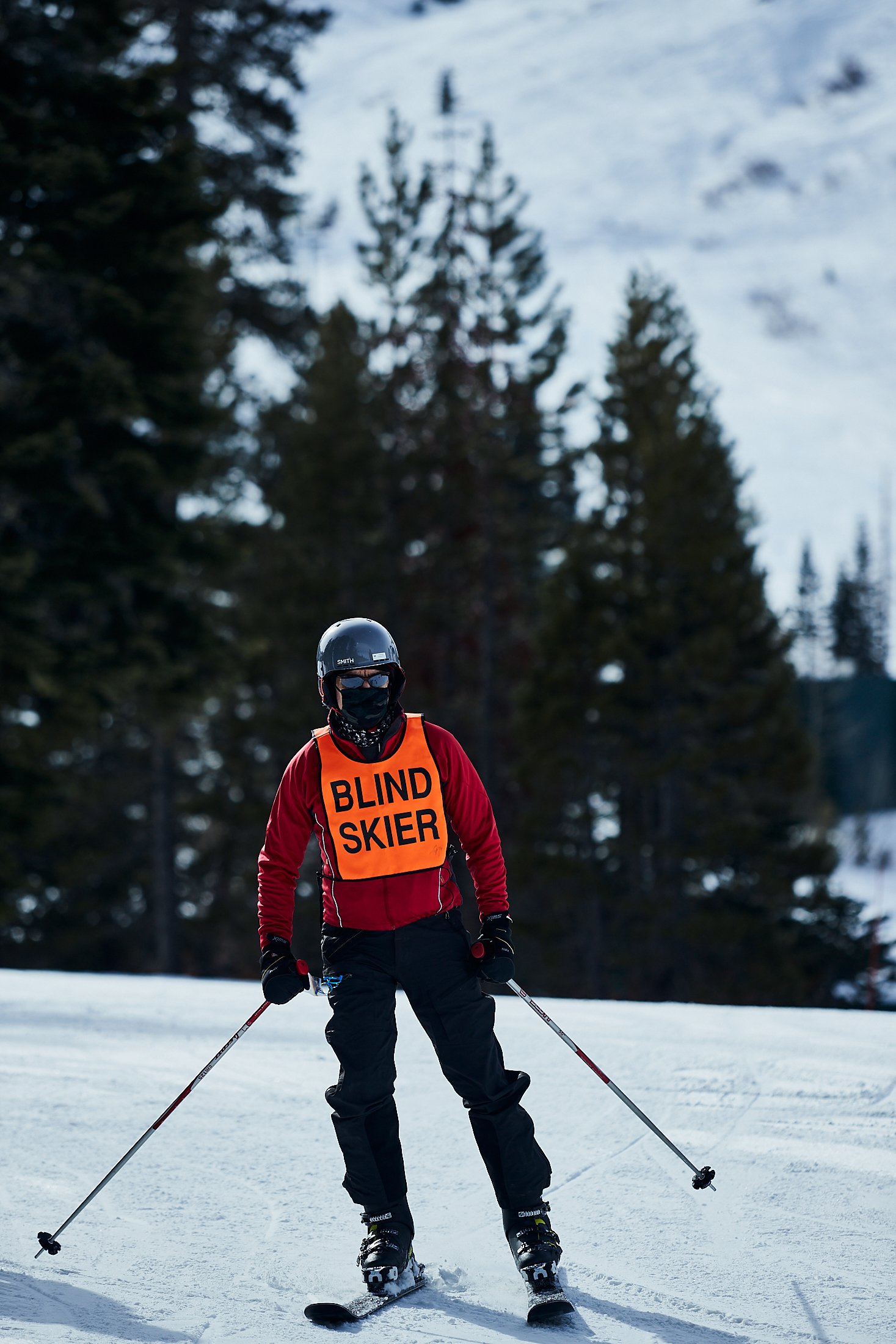Walt Raineri, wearing a longsleeve red top, black ski pants, and a blind skier vest, skis in Lake Tahoe.