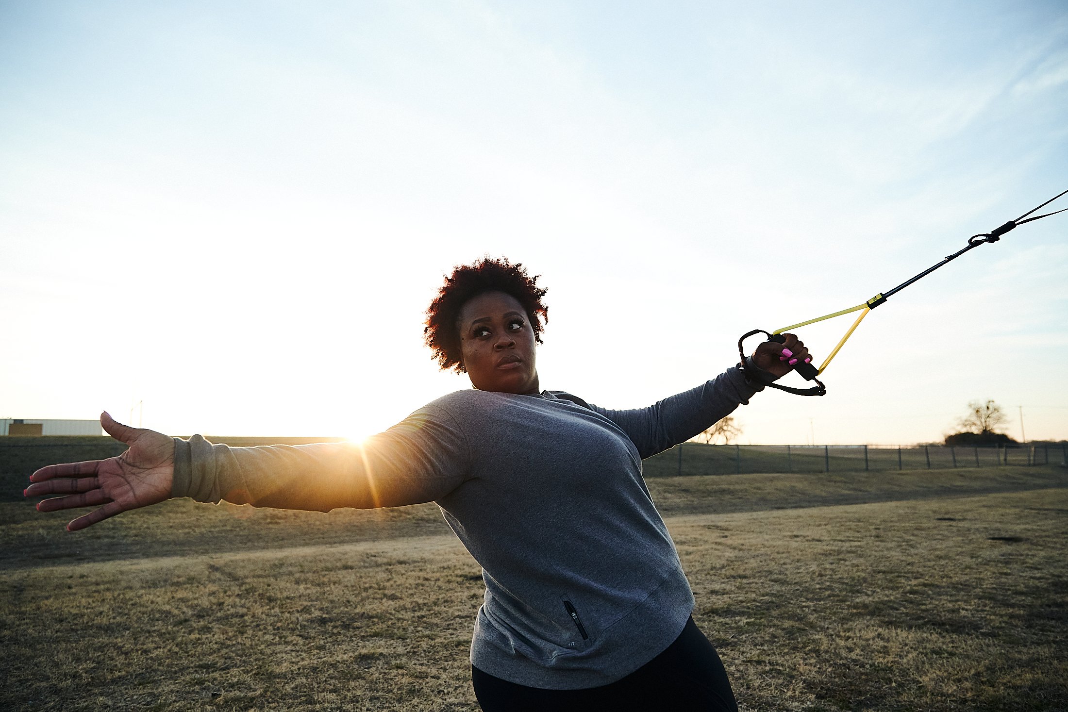 Michelle Carter, wearing a grey longsleeve shirt and leggings, warms up using a TRX Suspension Trainer